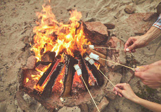 Outdoor sweet. Close up of campfire and people hands frying marshmallows at the beach